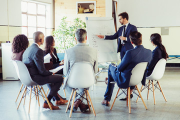 Thoughtful speaker pointing at whiteboard. Group of employees discussing ideas during presentation of new project at briefing. Business meeting concept