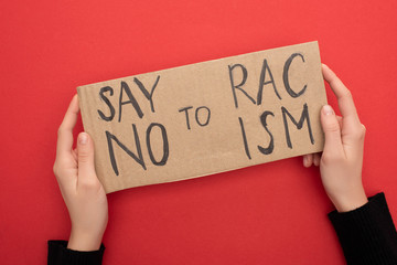 cropped view of woman holding carton placard with say no to racism lettering on red background