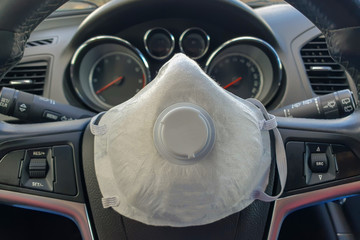 A white face shield to protect the human respiratory tract lies in the car on the steering wheel....