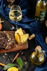 Sliced meat barbecue served on a wooden board,pineapple slices and a glass of white wine around