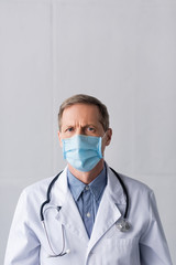 middle aged doctor in blue medical mask and white coat on grey