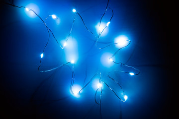 Top view of shining garland on wooden background in dark. Christmas backdrop with blue lights.