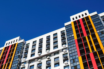 Modern building facade with windows, balconies and boxes for air conditioner on blue sky. Copy space, view at an angle.