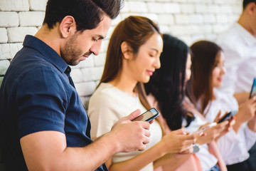 Group of happiness people standing together with white brick wall background all staring into their smartphones or cellphone