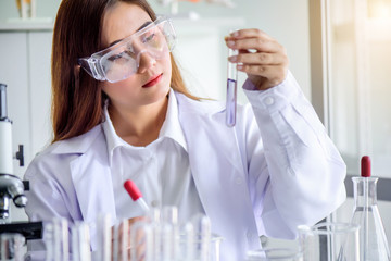 Attractive young Asian scientist woman lab technician assistant analyzing sample in test tube at laboratory. Medical, pharmaceutical and scientific research and development concept.