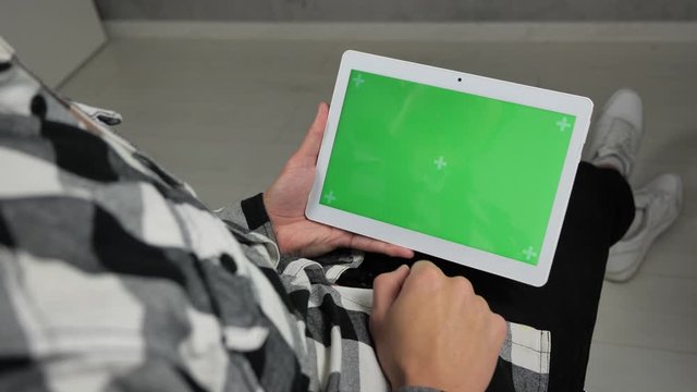 Man sitting on chair looking at digital tablet with green screen chroma key