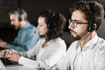 Concentrated bearded call center operator working. Thoughtful call center operators during working...