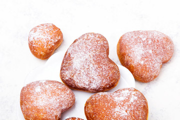 Homemade heart sheped donuts with powdered sugar on white background. Tasty doughnuts, copy space