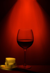 a glass of wine on a glass table with cheese on a wooden spoon in a red light