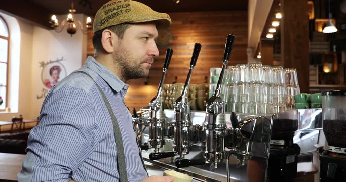 Medium shot of a vintage barista man tasting and drinking coffee. Tasting a cappuccino or espresso in a vintage coffee shop. Nearly not looking in the camera.