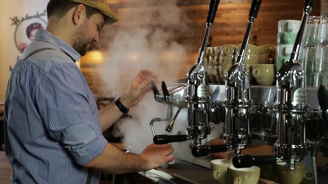 Medium shot of a smiling vintage barista creating a blast of steam on a professional coffee machine. SLOMO-version