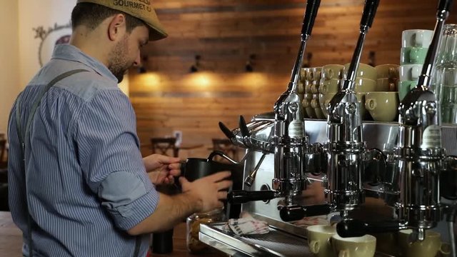 Medium shot of a smiling vintage barista creating a blast of steam on a professional coffee machine.