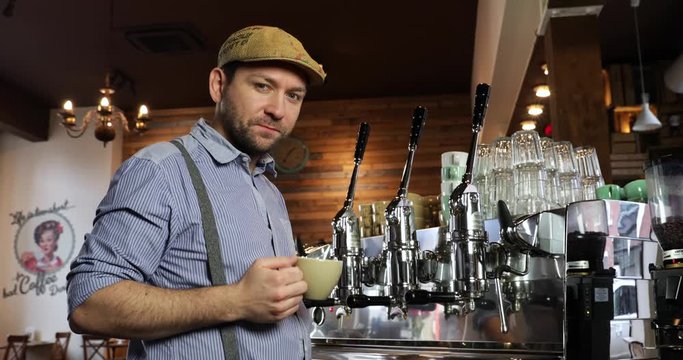 Medium shot of a vintage barista man tasting and drinking coffee. Tasting a cappuccino or espresso in a coffee shop while looking to the camera