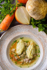 Soup with dill,celery root,carrots,cabbage and potatoes.Soup in a white bowl.Next to the bowl is cut potatoes,carrots and  dill.