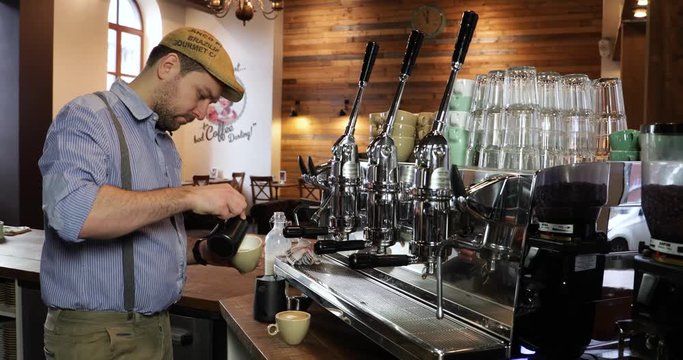 Vintage barista at work. Process of making coffee. Young man with a beard preparing a cappuccino on an authentic Italian coffee machine at a vintage coffee shop. Pouring fresh foaming milk in a cup.