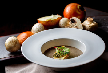 Mushroom soup in white bowl on a black background.On the table are mushrooms and onions.