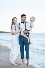 Beautiful young family of three walking along the sea shore. Father holds child on hands. Vertical frame