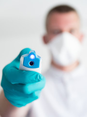 Jeune docteur avec gants et masque tenant un thermomètre à lecture optique