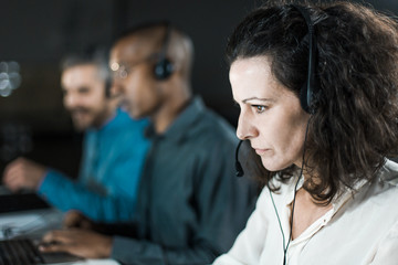 Focused mature call center operator looking at laptop screen. Serious curly woman working in office. Call center concept