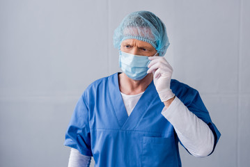 Fototapeta na wymiar mature doctor touching blue medical mask on grey