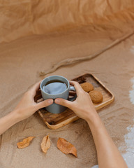 A mug of tea on a wooden tray, next to homemade cookies and spices. Background of sand and craft paper.