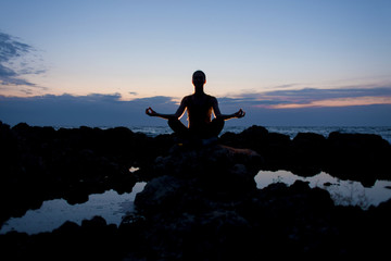 Yogi girl in lotus pose on the rocks near the sea at night