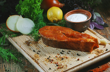 Pickled raw red fish lies on a light board with dill, lemon and seasonings.