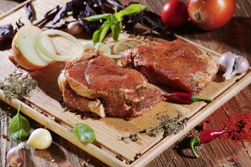 Pickled raw meat lies on a light board with tomatoes cherry, red pepper, basil, garlic and seasoning.