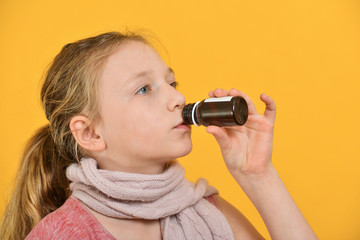 A sick child takes medicine, a girl drinks medicinal syrup from a bottle.