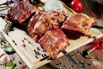 Pickled raw meat lies on a light board with onions, pepper,  garlic and seasoning.