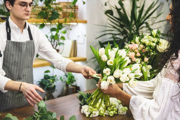Shopping at the store. Attractive male seller sells a bouquet of flowers in a flower shop and receives money.