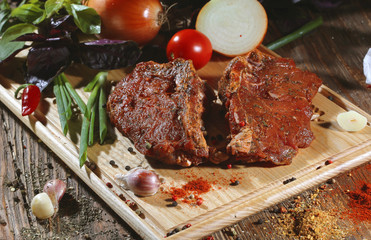 Pickled raw meat lies on a light board with tomatoes cherry, red pepper, onions, basil, garlic and seasoning.