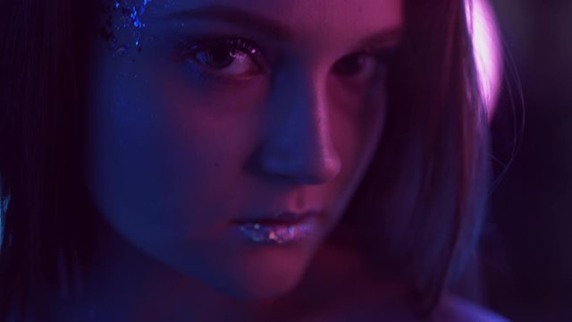 Color light portrait. Disco night. Woman face with glitter makeup in purple blue neon glow.