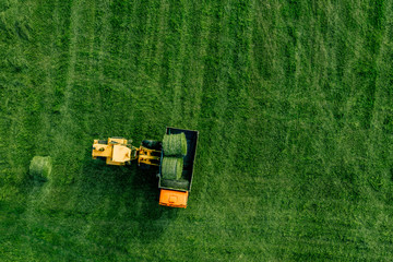 Aerial view of green grass harvest field with tractor moving hay bale