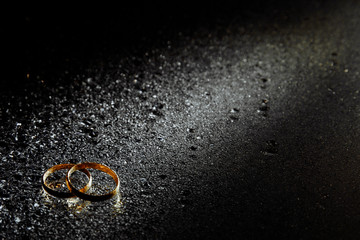 Two gold wedding rings as a symbol of family. The rings lie on top of each other illuminated by a path of light. Water drops are visible everywhere.