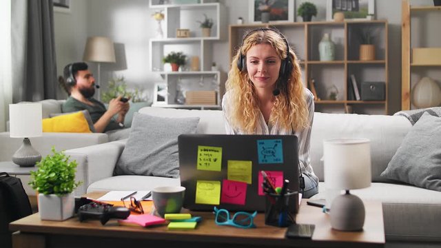 A young woman holds a video conference and her husband plays video games during quarantine