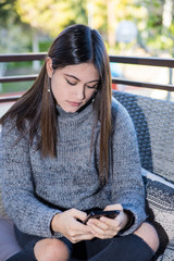 A teenager, sit in a terrace,  looking at her cell phone
