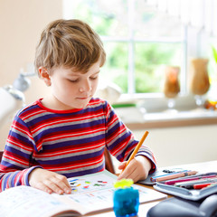 Hard-working happy school kid boy making homework during quarantine time from corona pandemic disease. Healthy child writing with pen, staying at home. Homeschooling concept