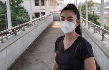 A Black shirt woman standing on putting on a respirator N95 mask to protect from airborne respiratory diseases as the flu covid-19 coronavirus PM2.5 dust and smog on the road burred background