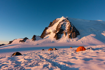 Colorful tents in snow at sunrise in Col du Midi, under Mont Blanc du Tacul, massif of Mont Blanc, Chamonix, French Alps