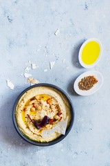 Classic hummus in a bowl with herbs, smoked paprika, olive oil and lettuce on a blue (gray) background. Healthy vegan food. A dish of Middle Eastern cuisine. Healthy eating concept.