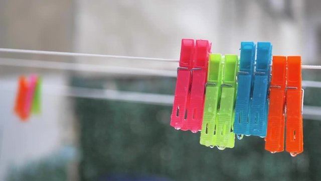 Pinzas de colgar ropa de colores colgadas en cuerda bajo lluvia en c&aacute;mara lenta