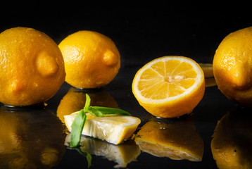 yellow  lemons with Basil on a wet black , half, slices and whole  citrus,  copy space
