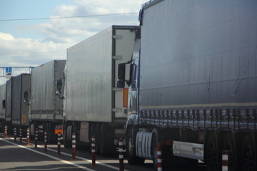 Fototapeta na wymiar A many van trucks with trailers queue row on asphalt road near control point rear side view at Sunny summer day, transit cargo shipping