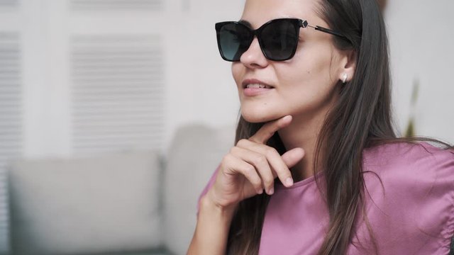 Portrait of beautiful woman in dark sunglasses in cafe, looking at camera