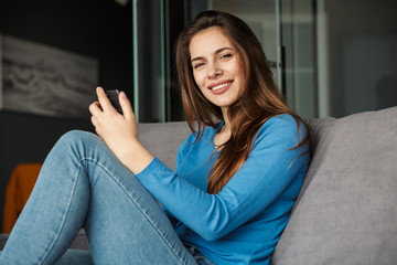 Obraz premium Image of joyful woman using cellphone and smiling while sitting on sofa