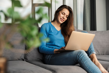 Obraz premium Image of happy woman using laptop and smiling while sitting on sofa