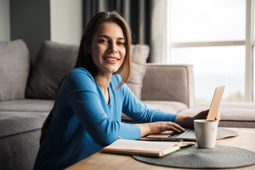 Image of happy woman using laptop and smiling while sitting on floor