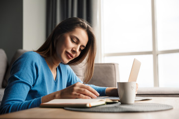 Image of happy woman using laptop and smiling while sitting on floor