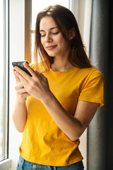 Image of pleased woman using mobile phone and smiling while standing